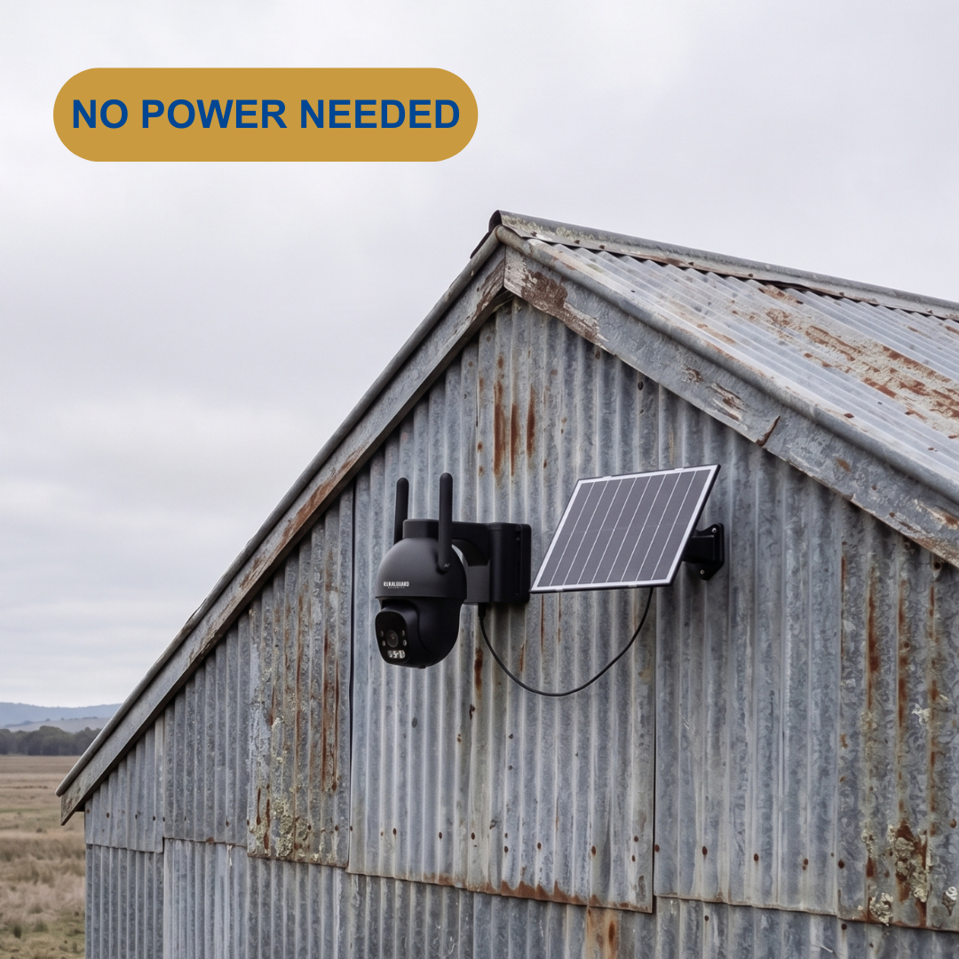 A black solar security camera with two antennas and an attached solar panel mounted on the corrugated metal gable of a rustic barn. An orange badge in the top left reads 'NO POWER NEEDED' against an overcast sky.